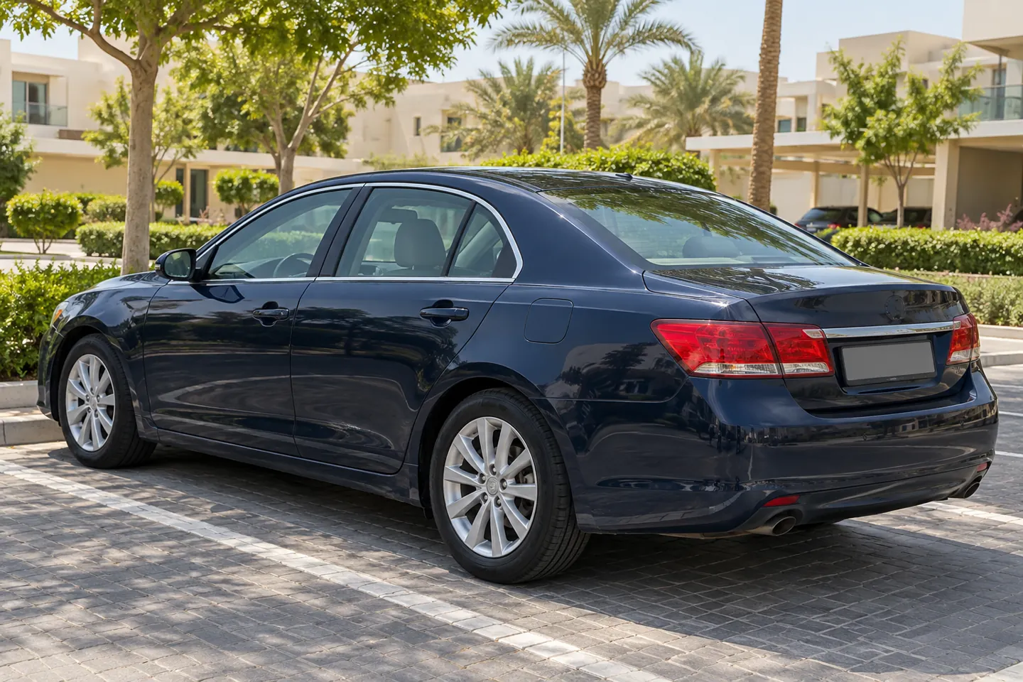 Dark-blue mid-2010s executive-style sedan with minor body wear viewed from the rear in landscaped Khalifa City-style community outdoor parking