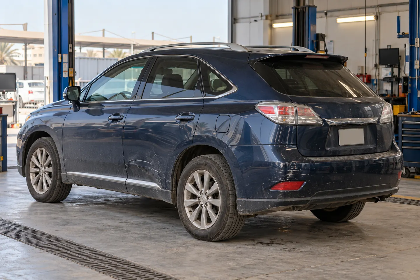 Used early-2010s dark-blue RX-style Lexus SUV with lower-door scratches and rear bumper wear in an independent UAE workshop