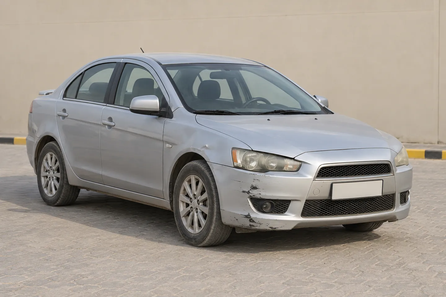 Used 2012 Lancer-style Mitsubishi sedan with bumper scrapes and a small front-fender dent at a UAE assessment forecourt