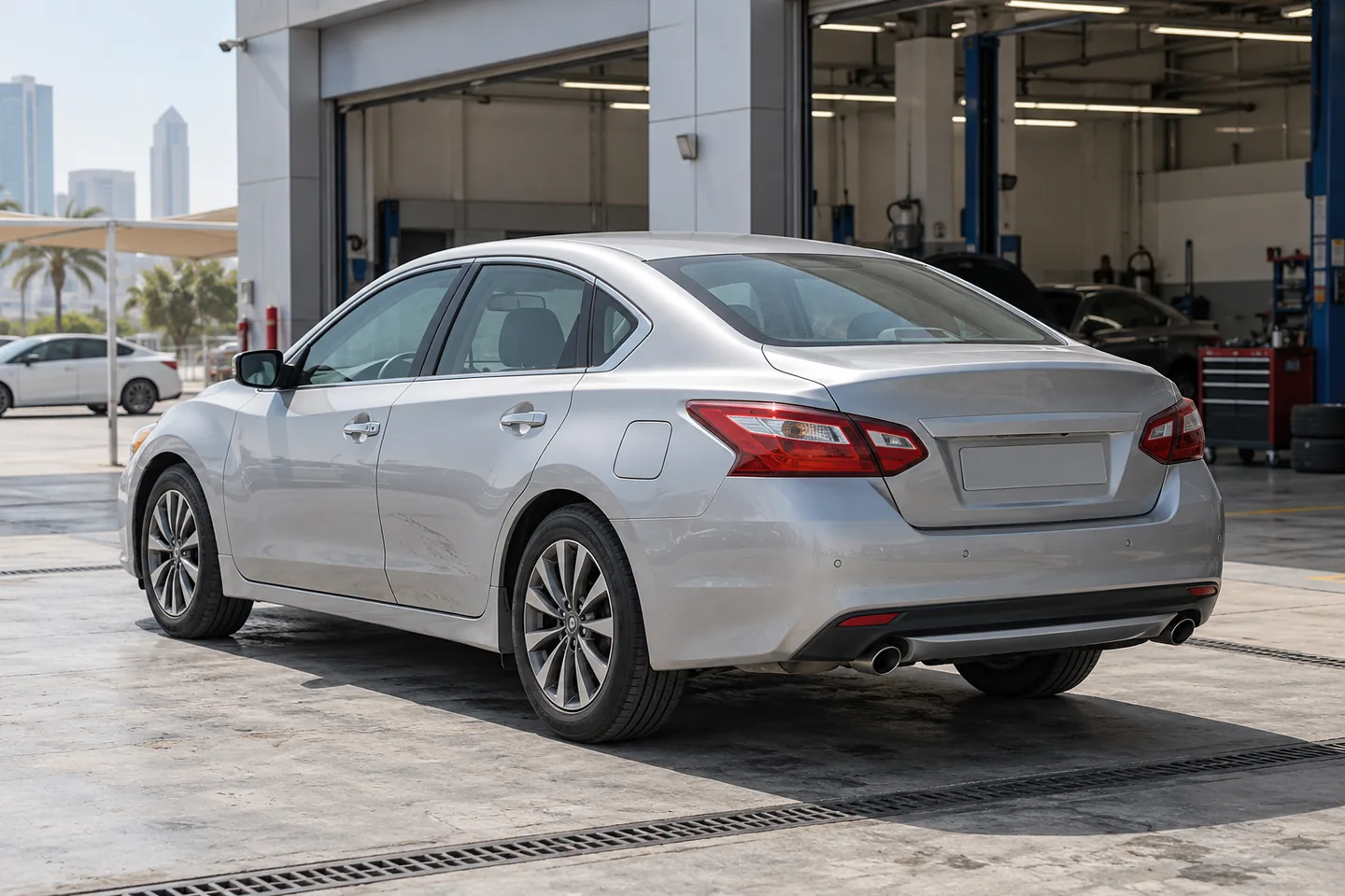 Silver Altima-style Nissan sedan with modest door wear awaiting assessment outside a UAE workshop in soft morning daylight